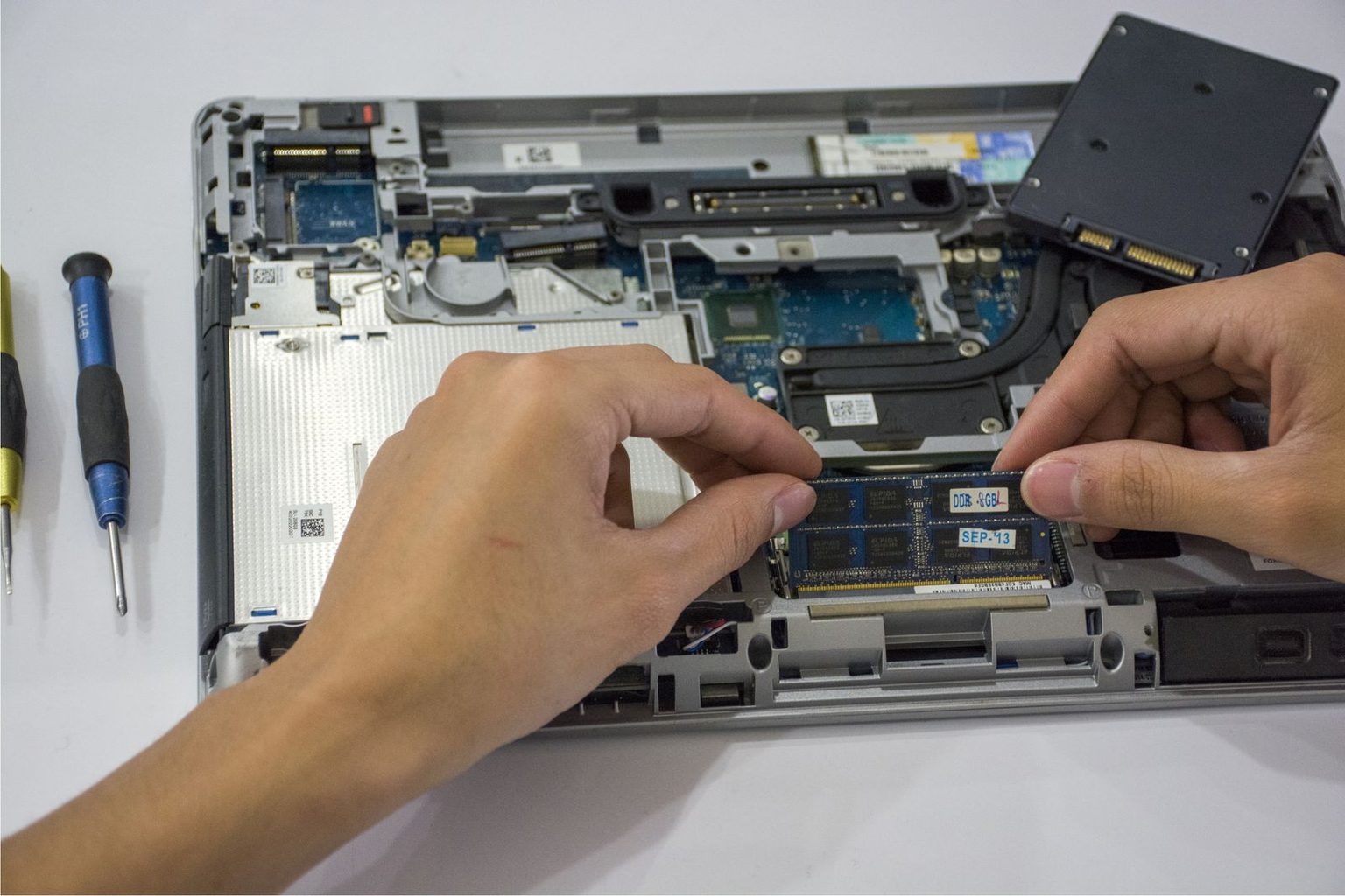 Deux mains installent une barrette de mémoire dans un ordinateur portable ouvert, à l'atelier Mac-PC-Services.